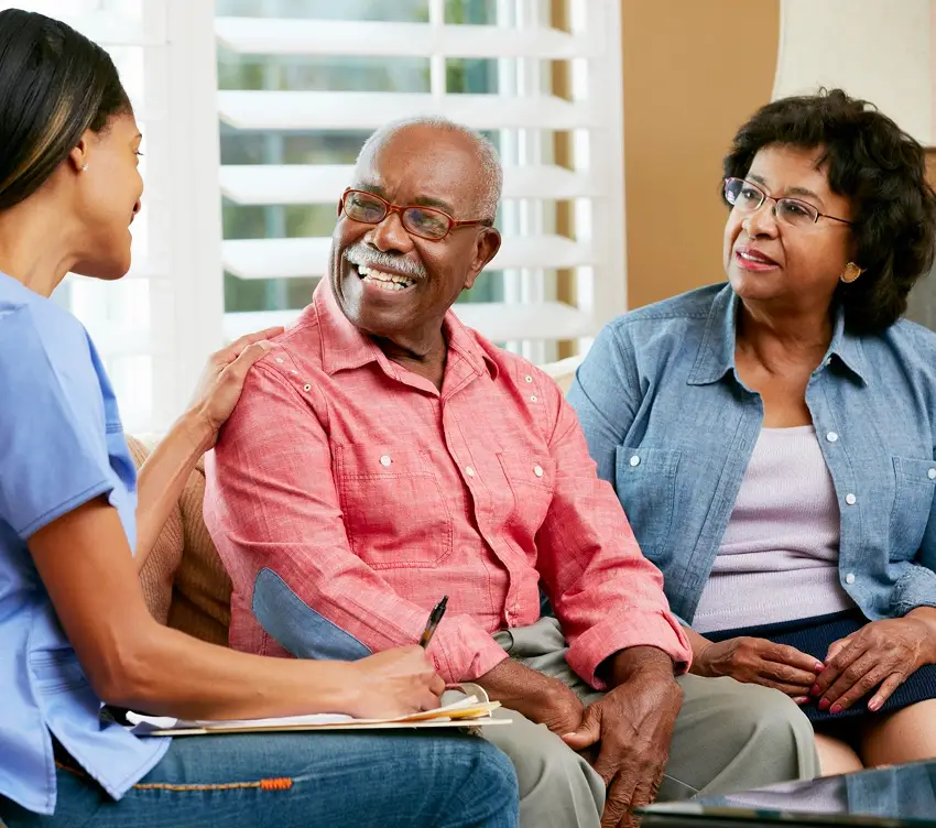A caregiver talking with an elderly couple in a home setting.